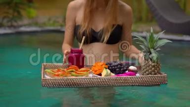 一位年轻的女游客在私人<strong>游泳</strong>池的一张漂浮的桌子上有自己的私人早餐。 热带海滩